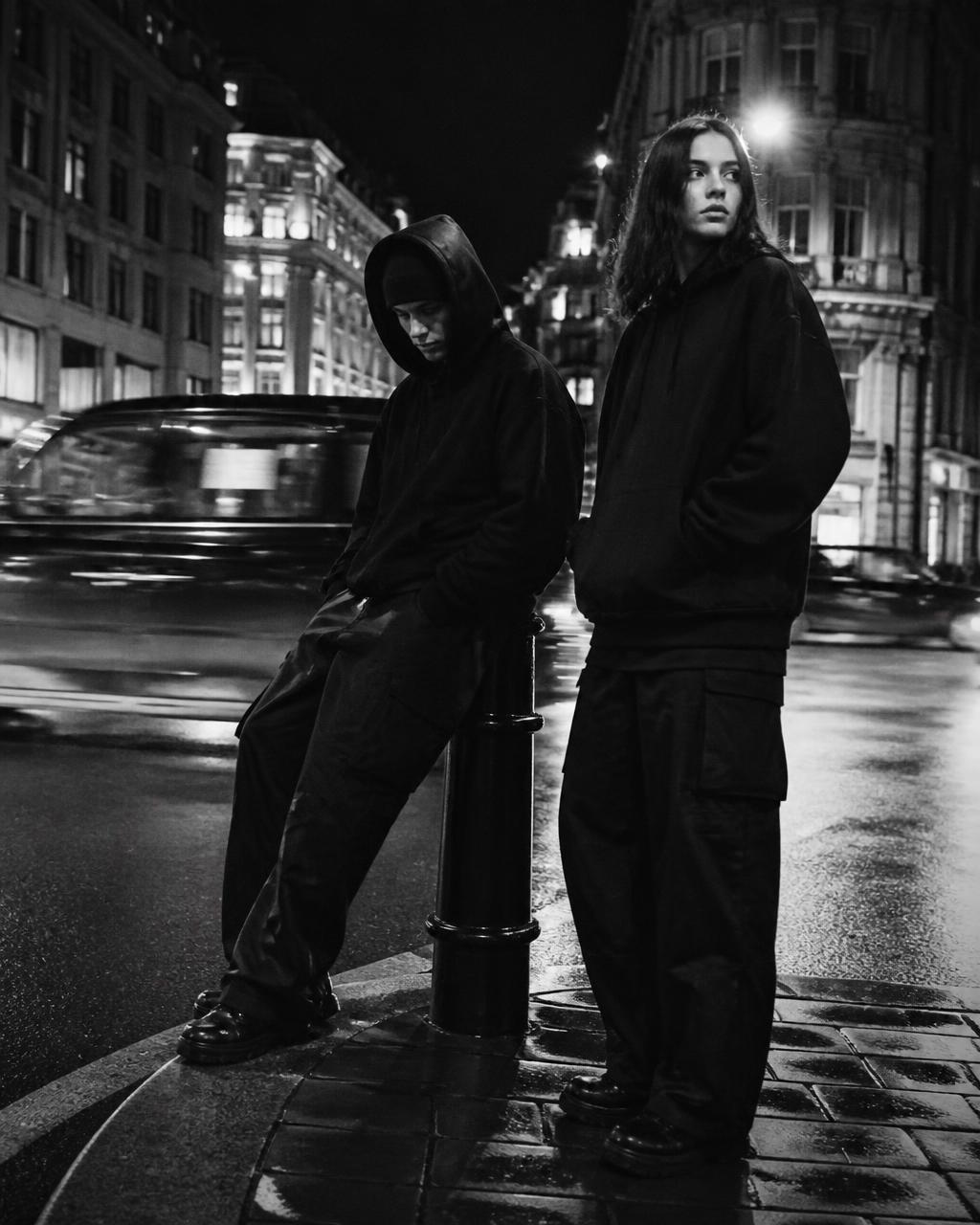 Two figures in black streetwear on a wet London street at night