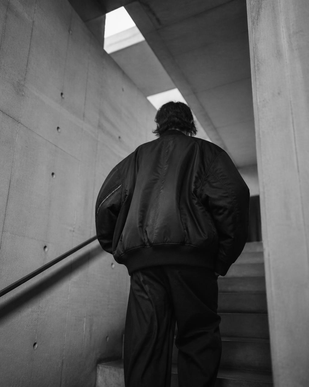 Model in an oversized bomber jacket on a concrete stairwell